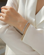 Load image into Gallery viewer, Close-up of a person wearing Eternelle Princesse Moissanite Tennis Bracelet on a white outfit
