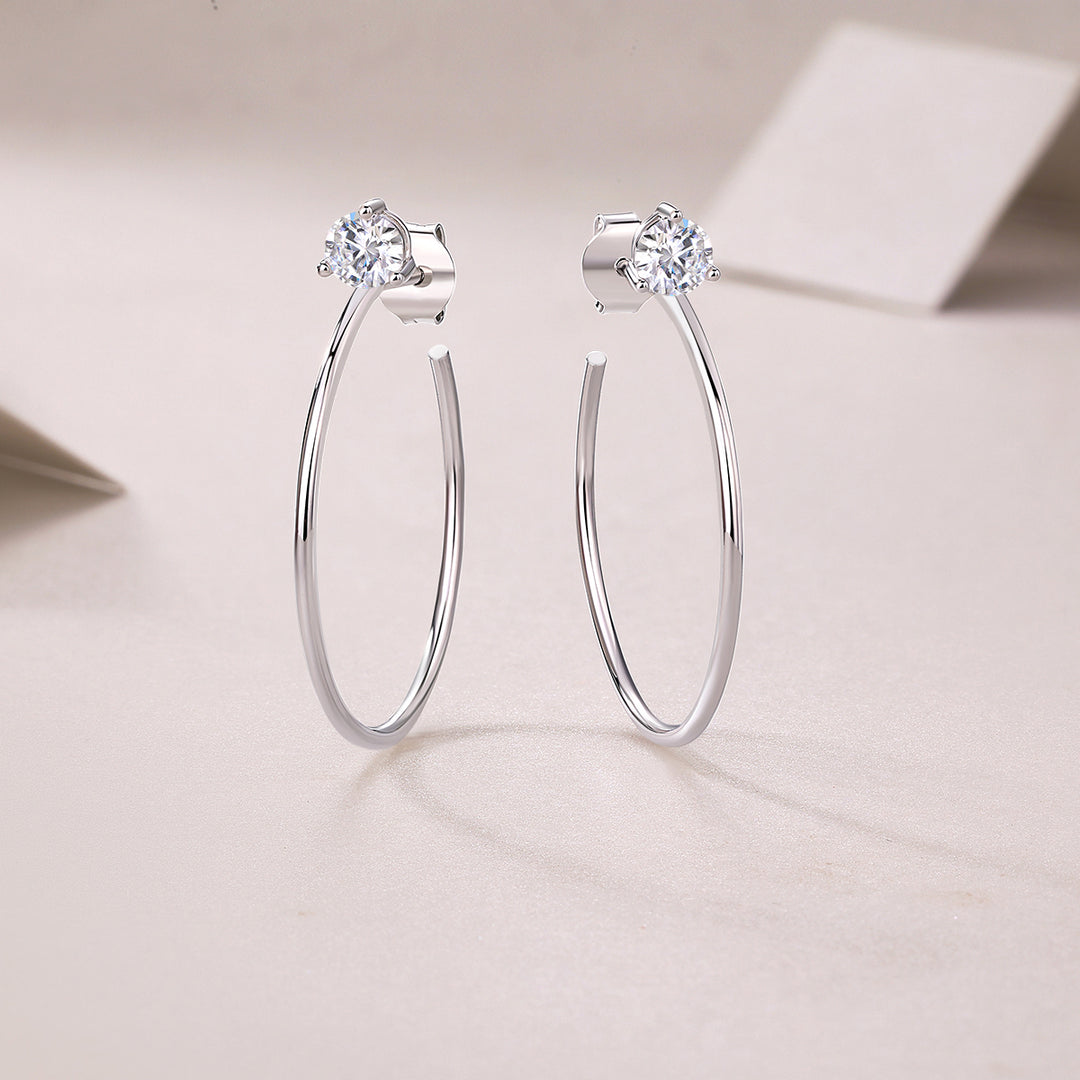 A pair of silver hoop earrings with round-cut moissanite stones set in a three-prong setting.
