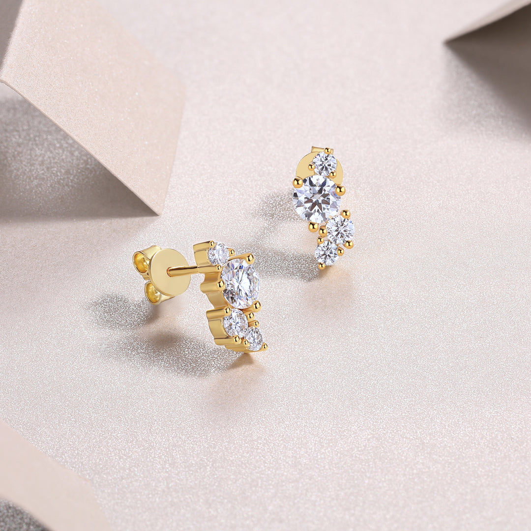 A pair of gold-plated round-cut moissanite earrings with a cluster design, displayed on a beige surface.
