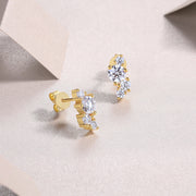 A pair of gold-plated round-cut moissanite earrings with a cluster design, displayed on a beige surface.