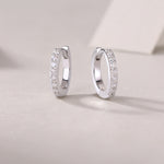 Load image into Gallery viewer, A pair of silver hoop earrings with round-cut moissanite stones set in a pavé pattern on a white surface.
