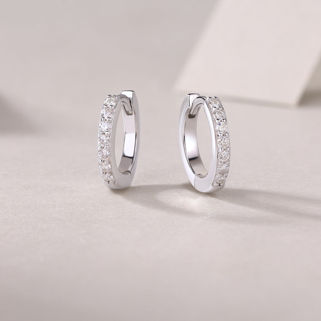 A pair of silver hoop earrings with round-cut moissanite stones set in a pavé pattern on a white surface.
