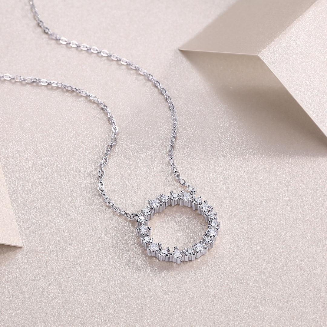 A circular sterling silver pendant necklace adorned with round-cut moissanite stones, displayed on a beige background.
