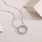 A circular sterling silver pendant necklace adorned with round-cut moissanite stones, displayed on a beige background.