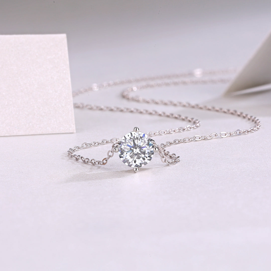 A classic round-cut moissanite stone necklace with a four-prong setting, displayed against a white background.