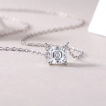 Load image into Gallery viewer, Éclat Cube Moissanite Necklace featuring a square-shaped Asscher-cut moissanite stone with a four-prong setting, displayed against a neutral background.
