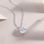 Load image into Gallery viewer, A round-cut moissanite stone, bezel set, hanging on a silver chain necklace displayed on a neutral background.
