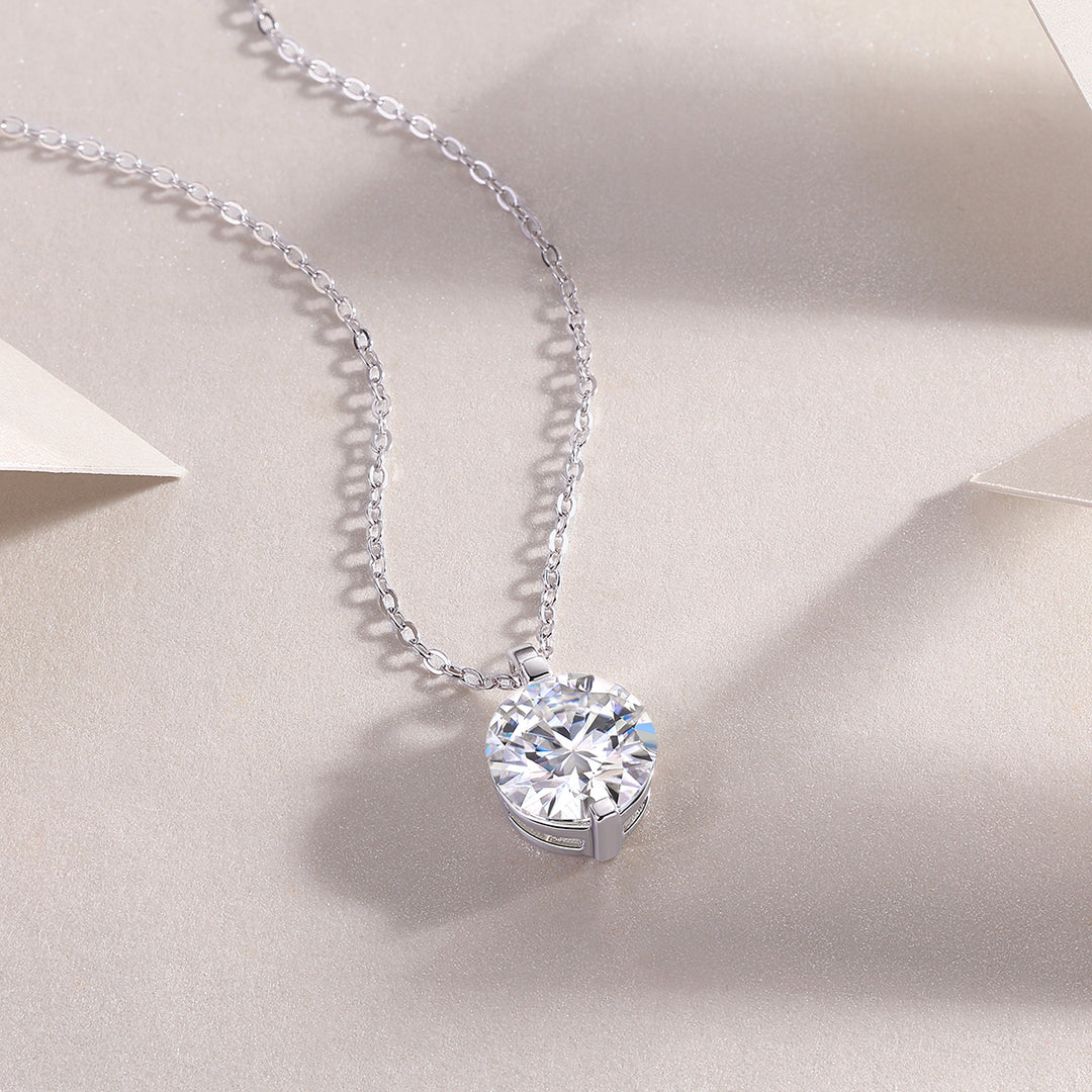 A round-cut moissanite stone, bezel set, hanging on a silver chain necklace displayed on a neutral background.