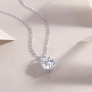 A round-cut moissanite stone, bezel set, hanging on a silver chain necklace displayed on a neutral background.
