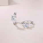 Load image into Gallery viewer, A pair of Éclat Solitaire Moissanite Huggie Earrings made with sterling silver and featuring round-cut moissanite stones, displayed against a neutral background.
