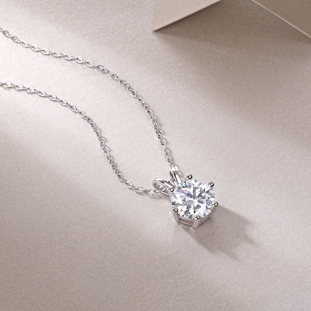 A solitaire moissanite necklace with a round-cut stone in a six-prong setting, displayed on a chain against a neutral background.
