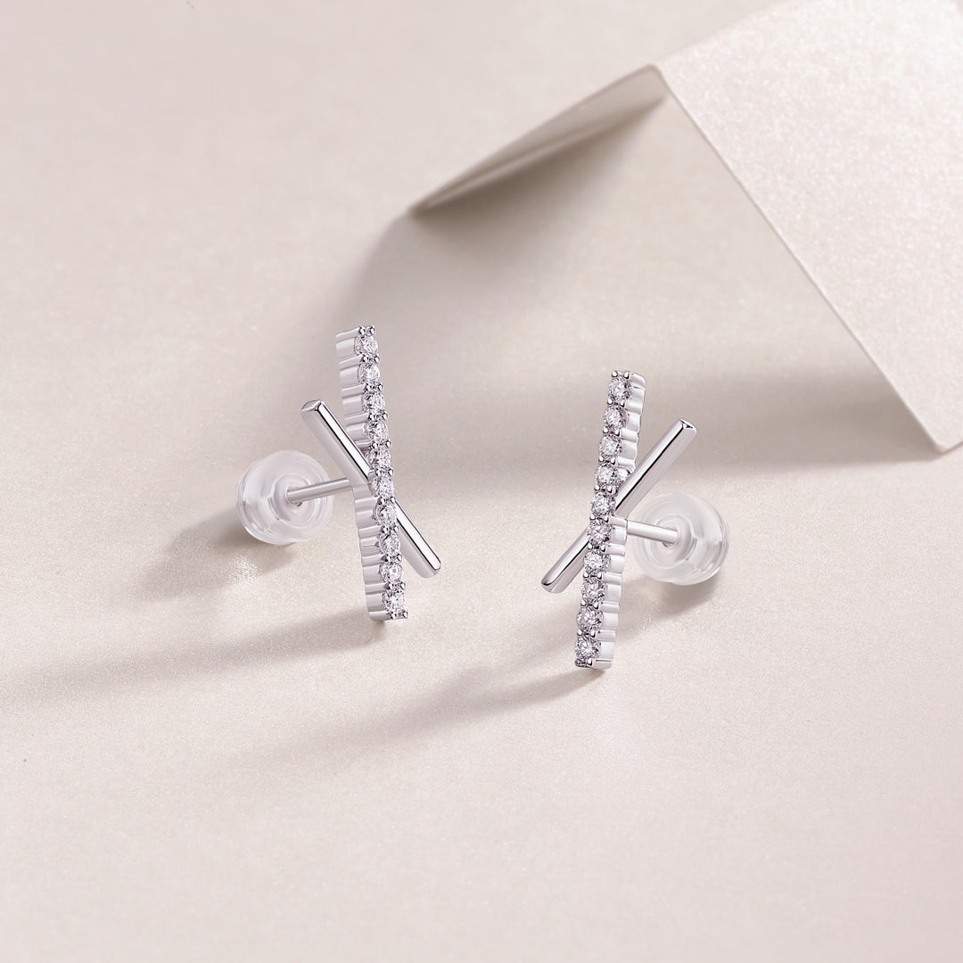 A pair of silver earrings with a contemporary X-shaped design and round-cut moissanite stones, displayed on a pale surface.