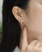 Load image into Gallery viewer, Close-up of an ear wearing Éternelle Brillance Huggie Moissanite Earrings
