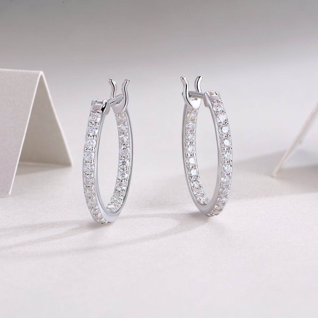 A pair of silver hoop earrings with round-cut moissanite stones set in a double-plated band, displayed on a white surface.