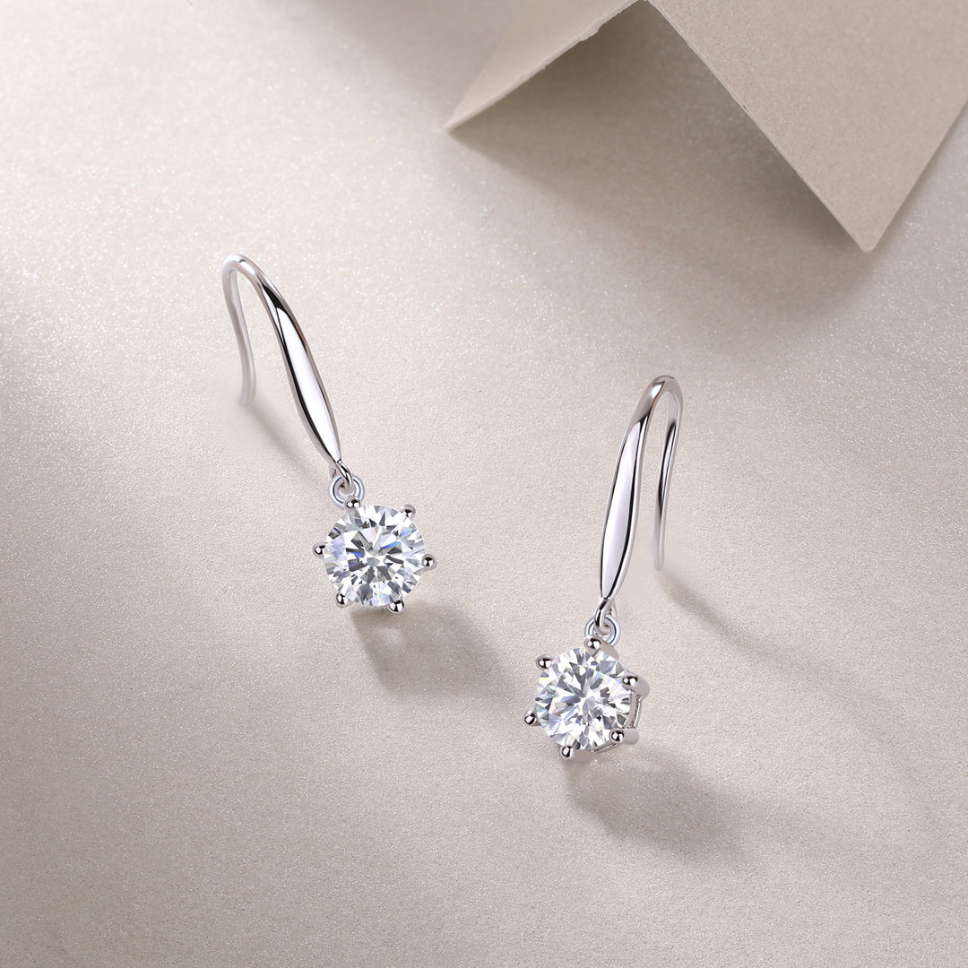 A pair of silver hoop earrings with round-cut moissanite stones, displayed against a beige background.