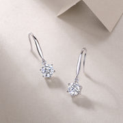 A pair of silver hoop earrings with round-cut moissanite stones, displayed against a beige background.